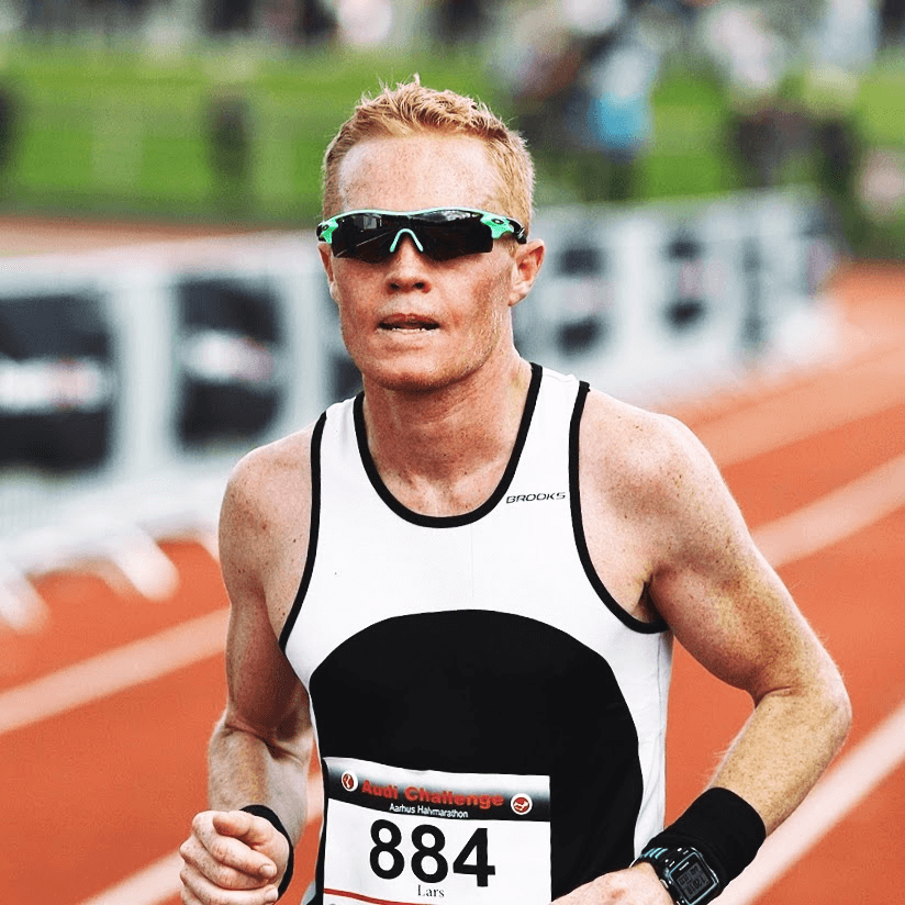 Athlete running on a track, wearing sunglasses, a black and white tank top, and a race bib with the number 884. The mood is focused and determined.