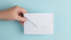 Hand holding a letter on a pale blue background.