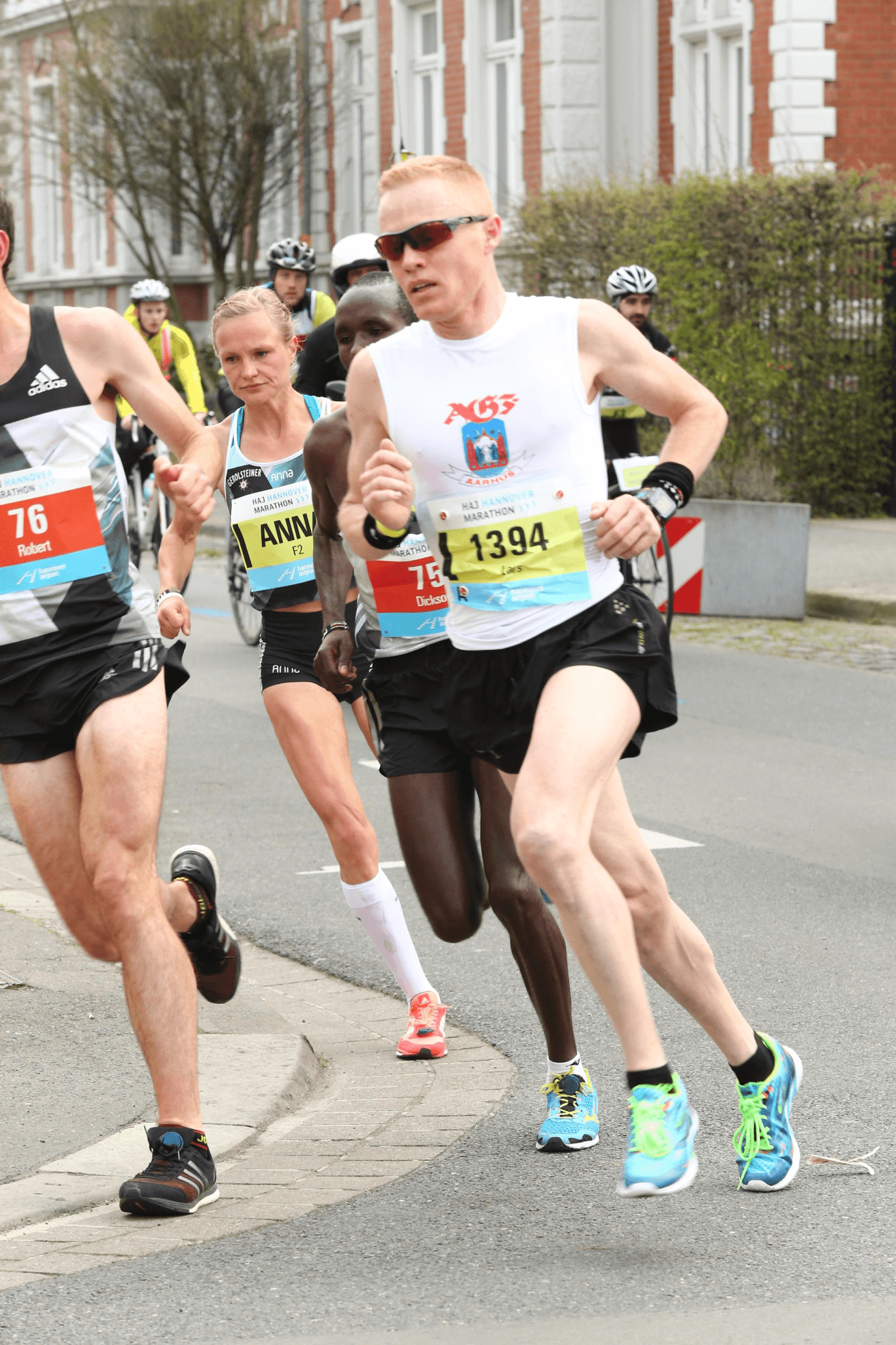 Runners in a marathon rounding a bend on a city street. They appear focused and determined, wearing numbered bibs and bright athletic gear.