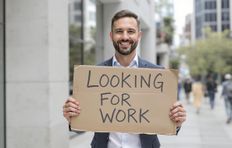 A man holding a sign stating "Looking for work," indicating he is seeking employment opportunities.